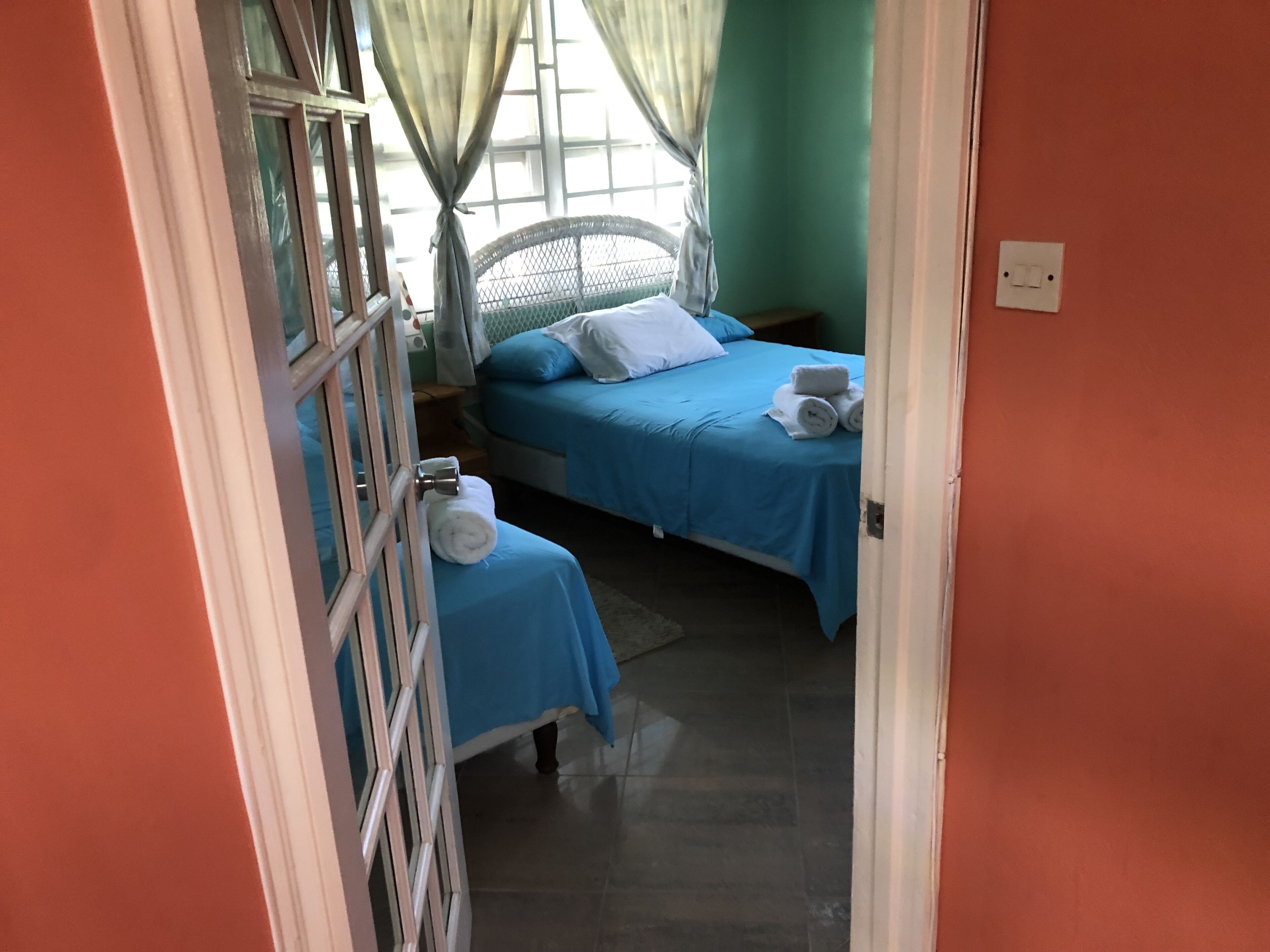 A room with two beds, each with blue bedding and white pillows. There are towels on the beds and a small table with a lamp.