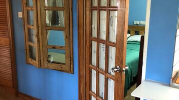 Une pièce avec une porte en bois, une fenêtre et un lit recouvert d’une couverture verte.