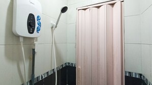 A bathroom with a white hand dryer, a showerhead, and a wooden door.