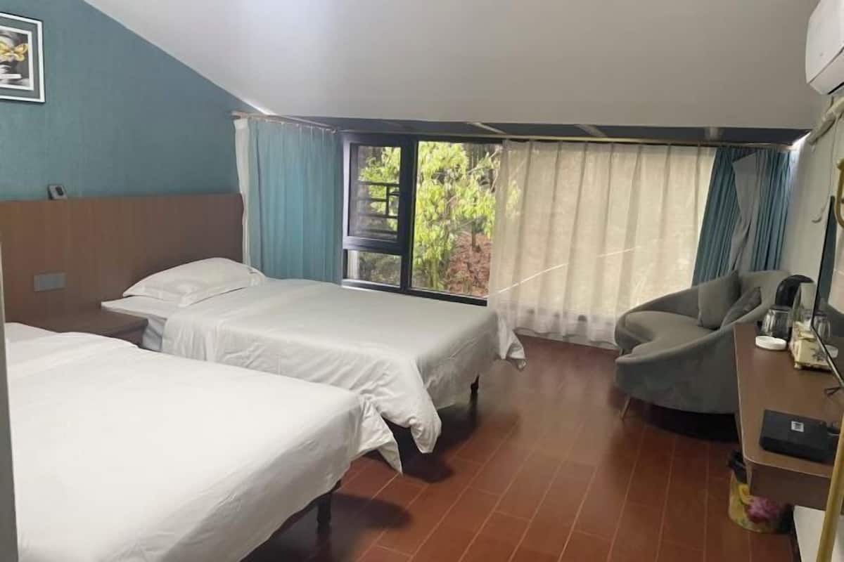 Quarto de hotel com duas camas, um sofá, uma escrivaninha e uma janela grande com cortinas.