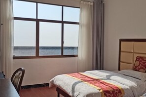 A hotel room with a large window offering a view of the sea, a bed with a patterned bedspread, and a wooden nightstand. - Fulin Leisure Inn (Hengyang)