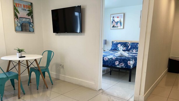 Une petite pièce propre, avec un lit, une télévision, une table avec des chaises et une porte donnant sur une autre pièce.