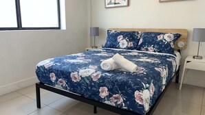 Un lit bien fait, avec une couvre-lit à motifs floraux, une tête de lit en bois et deux lampes de chevet.