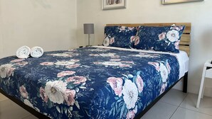Une chambre à coucher avec une couvre-lit à motifs floraux, une tête de lit en bois et deux œuvres d’art encadrées accrochées au mur.