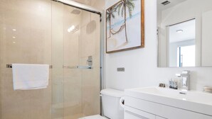 Une salle de bain moderne avec une douche à parois de verre, des toilettes et un lavabo blanc avec un miroir au-dessus.
