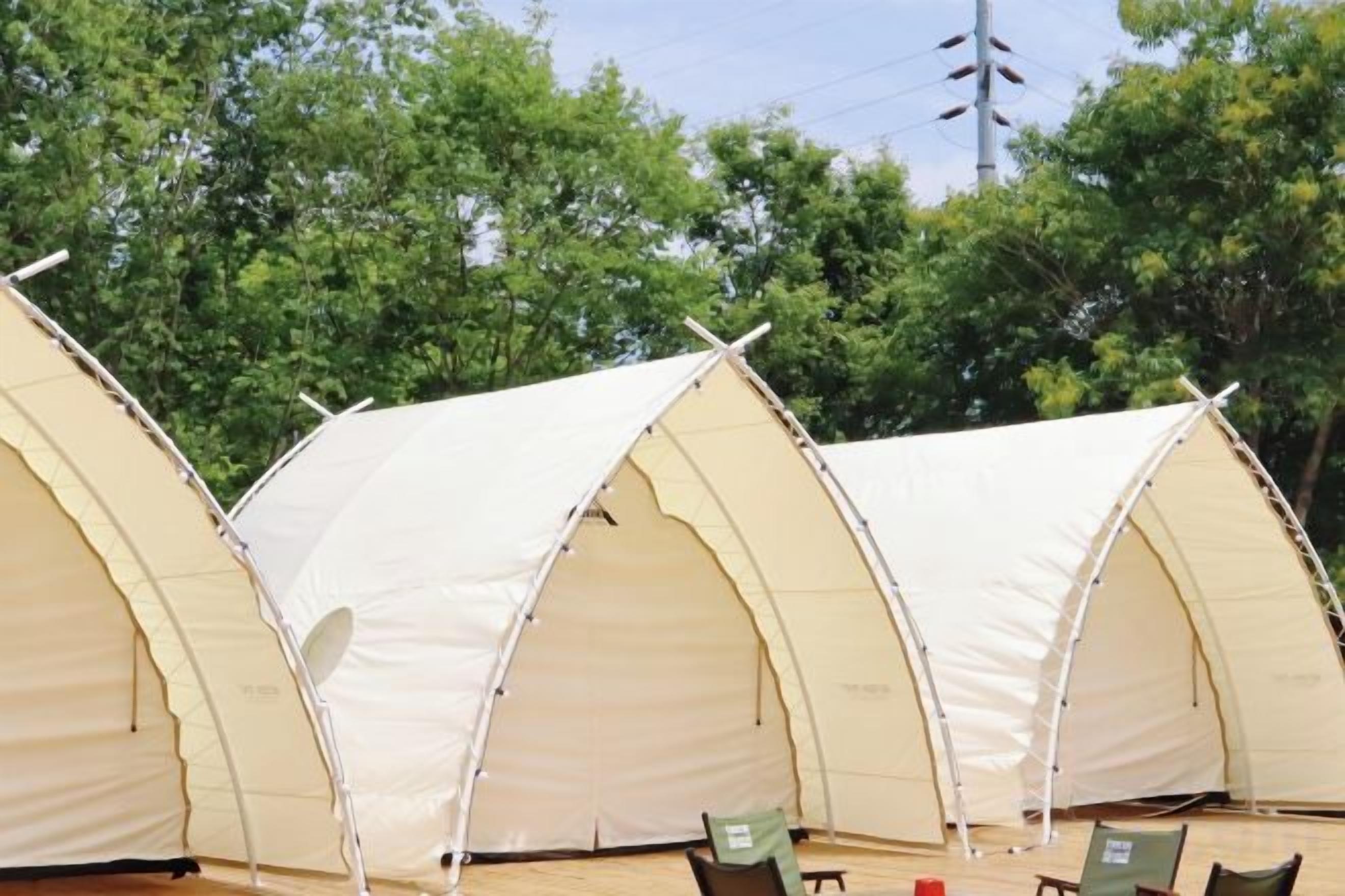 Una hilera de tres grandes tiendas tipo cúpula, de color beige y techo plano, dispuestas en fila sobre una terraza de madera.