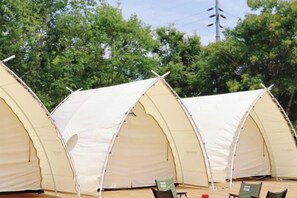 A row of three large, beige, dome-shaped tents with a flat roof, arranged in a row on a wooden deck.