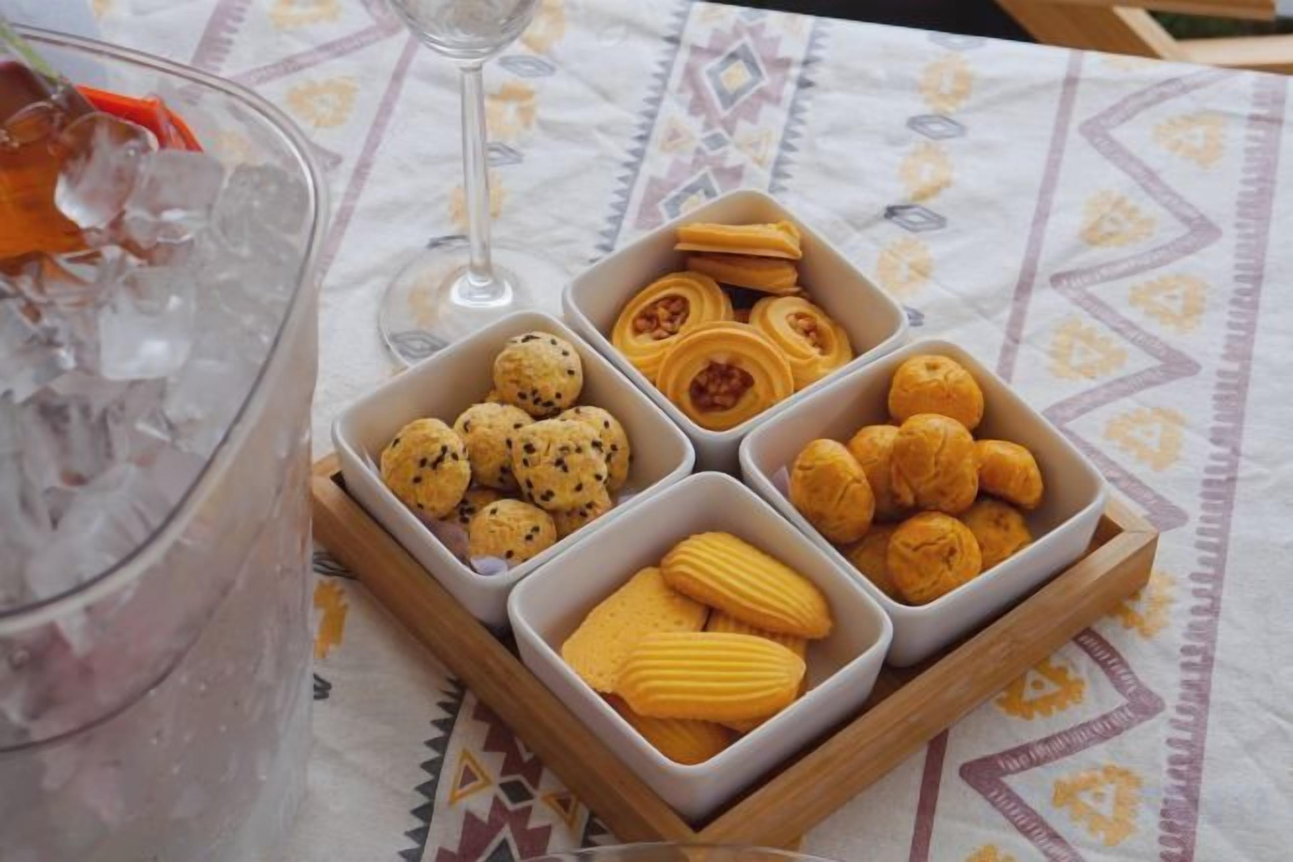 Un tavolo con un bicchiere di bevanda fredda, un bicchiere da vino e un vassoio di biscotti assortiti.
