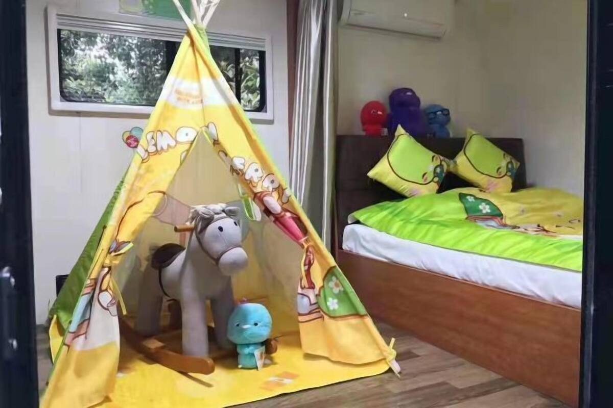 Een kinderkamer met een speeltent met tekenfilms, een bed met groene beddengoed en kleurrijke kussens.