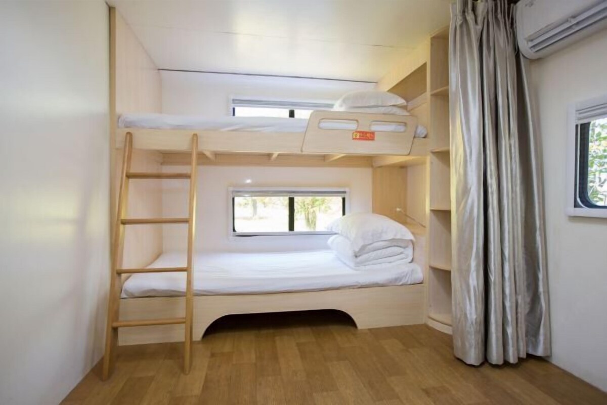 Une chambre avec un lit superposé, une échelle, une fenêtre et un rideau.