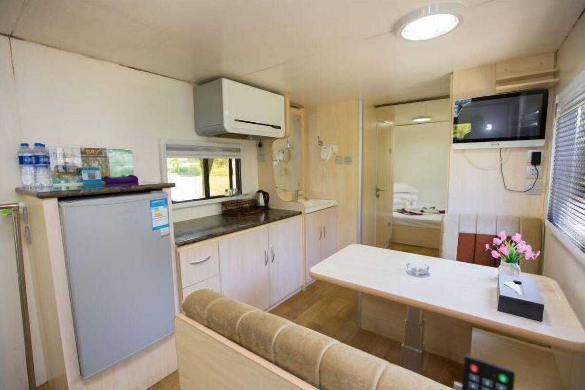 Een compacte camperkeuken met een koelkast, een magnetron, een spoelbak en een klein eethoekje.