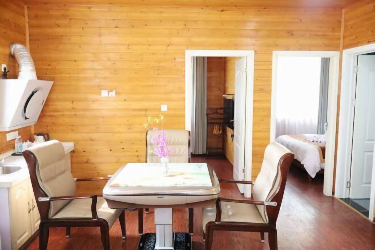 Een houten blokhut van binnen met een eettafel, twee stoelen, een klein keukenhoekje en een slaapkamer met een bed.