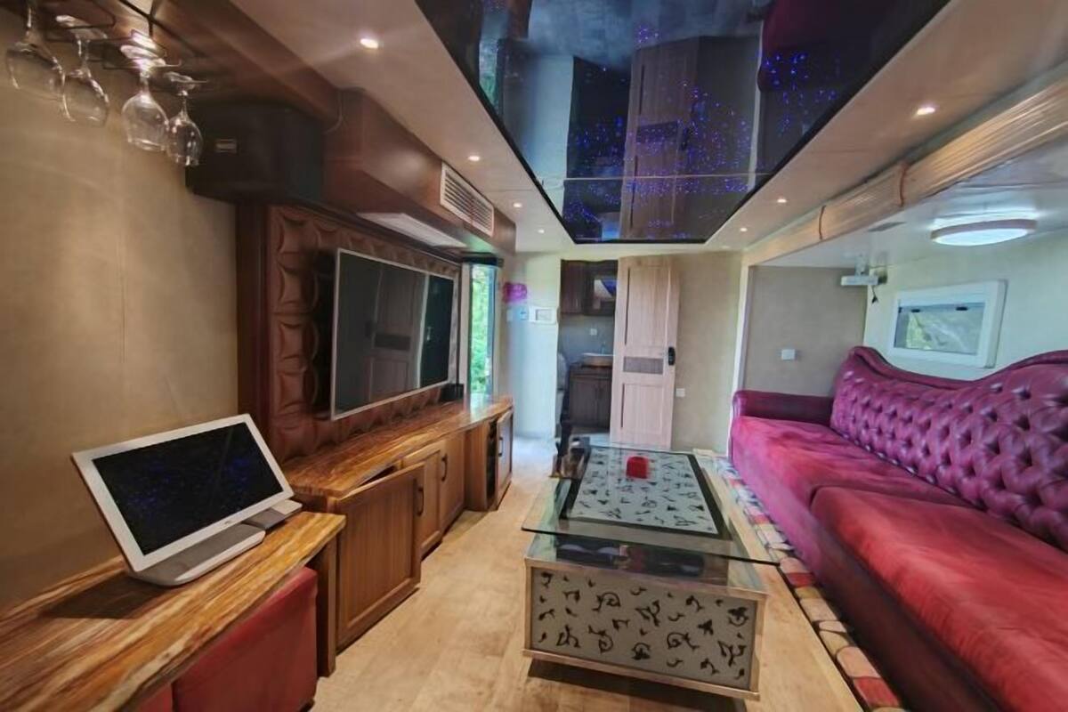 Een moderne woonkamer met een flatscreen televisie, een salontafel met glazen blad, een rode bank en een sterrenhemel verlichting in het plafond.