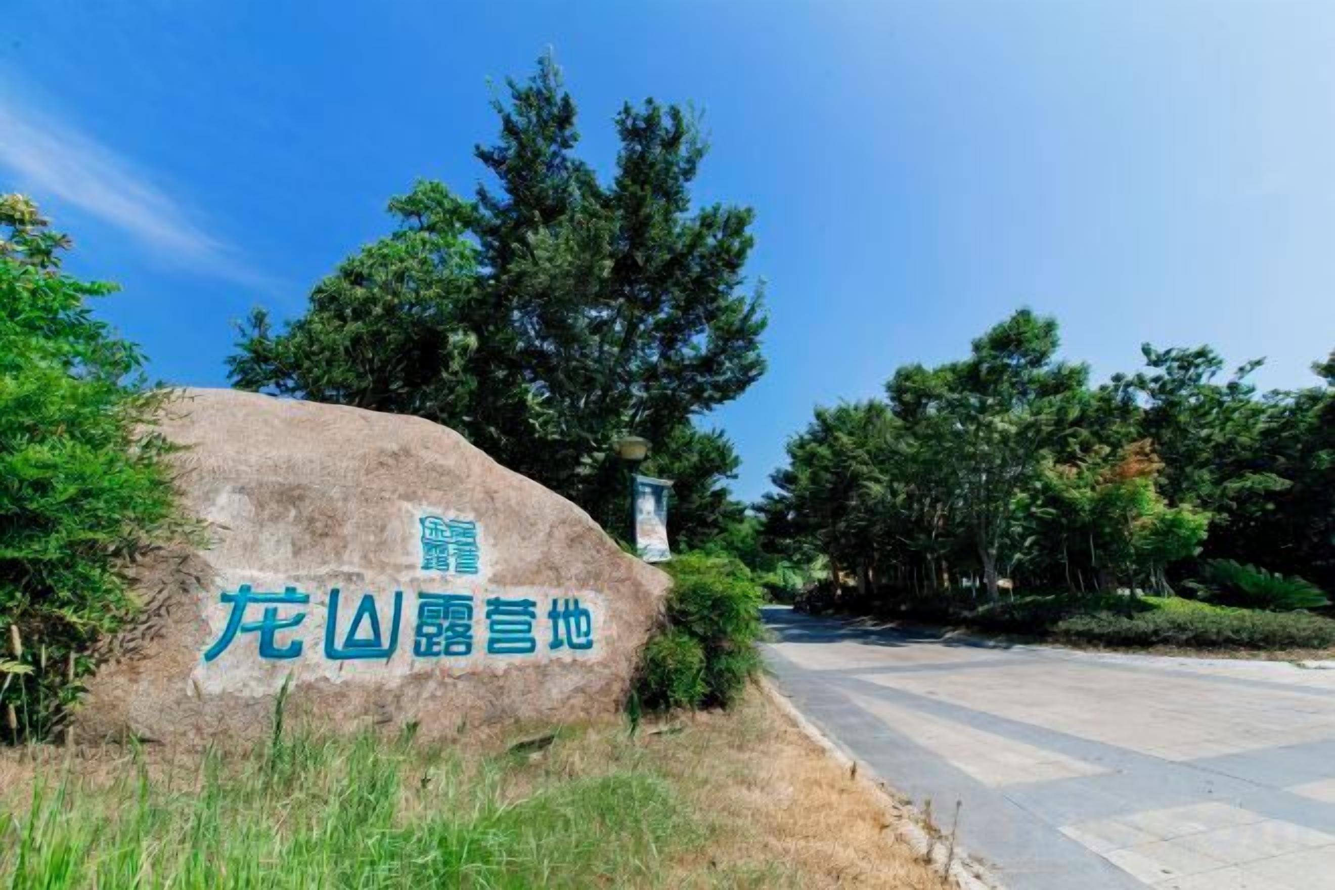 A large rock with text, surrounded by trees and a clear sky.