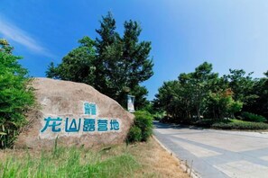 A large rock with text, surrounded by trees and a clear sky.