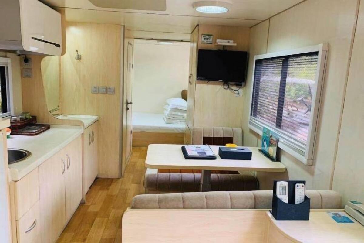 Een compact kampeerwageninterieur met een kitchenette, een eethoek, een zithoek en een aan de muur bevestigde televisie.