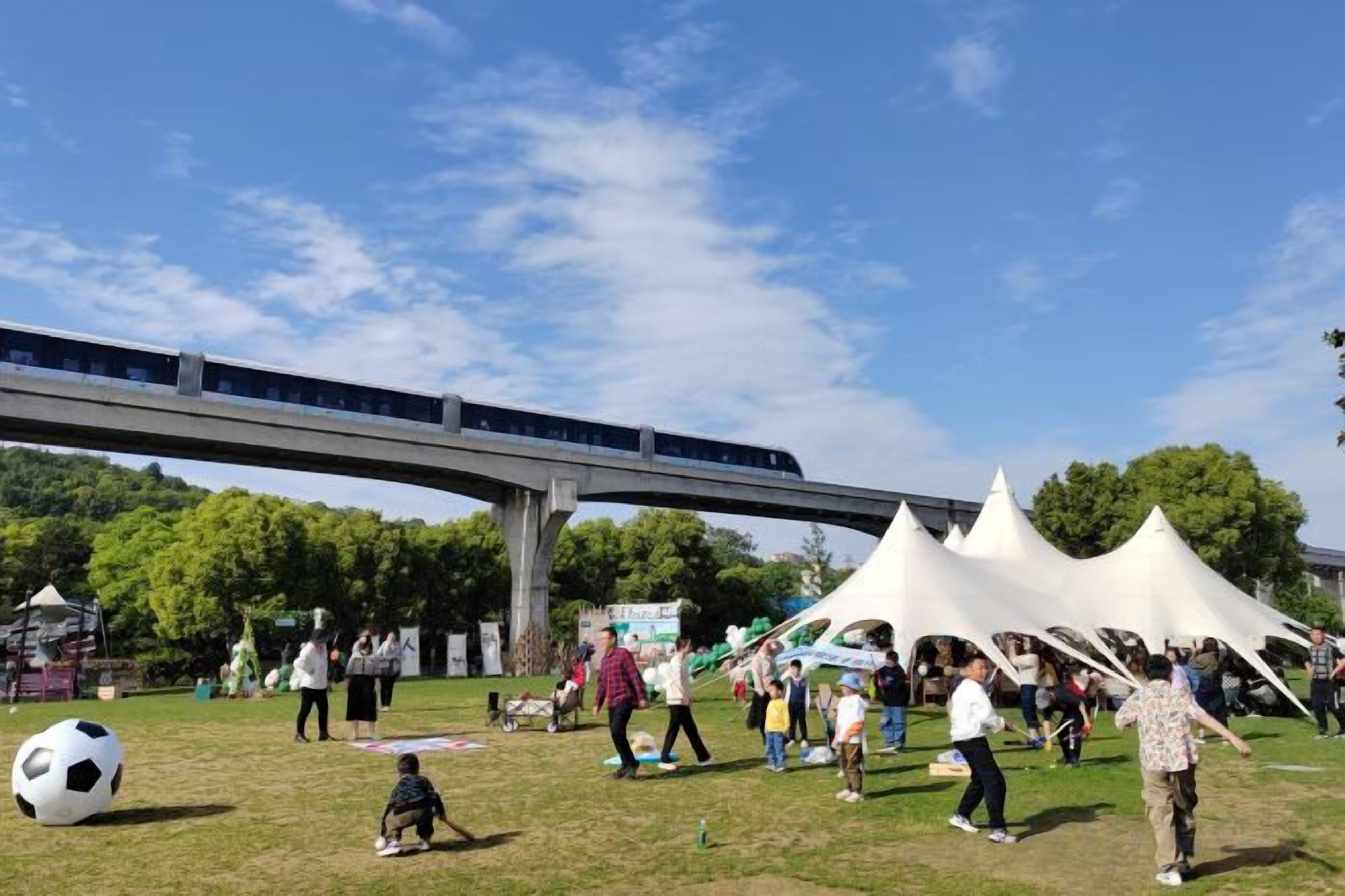 An outdoor event with tents and people, a soccer ball, and a train bridge in the background.