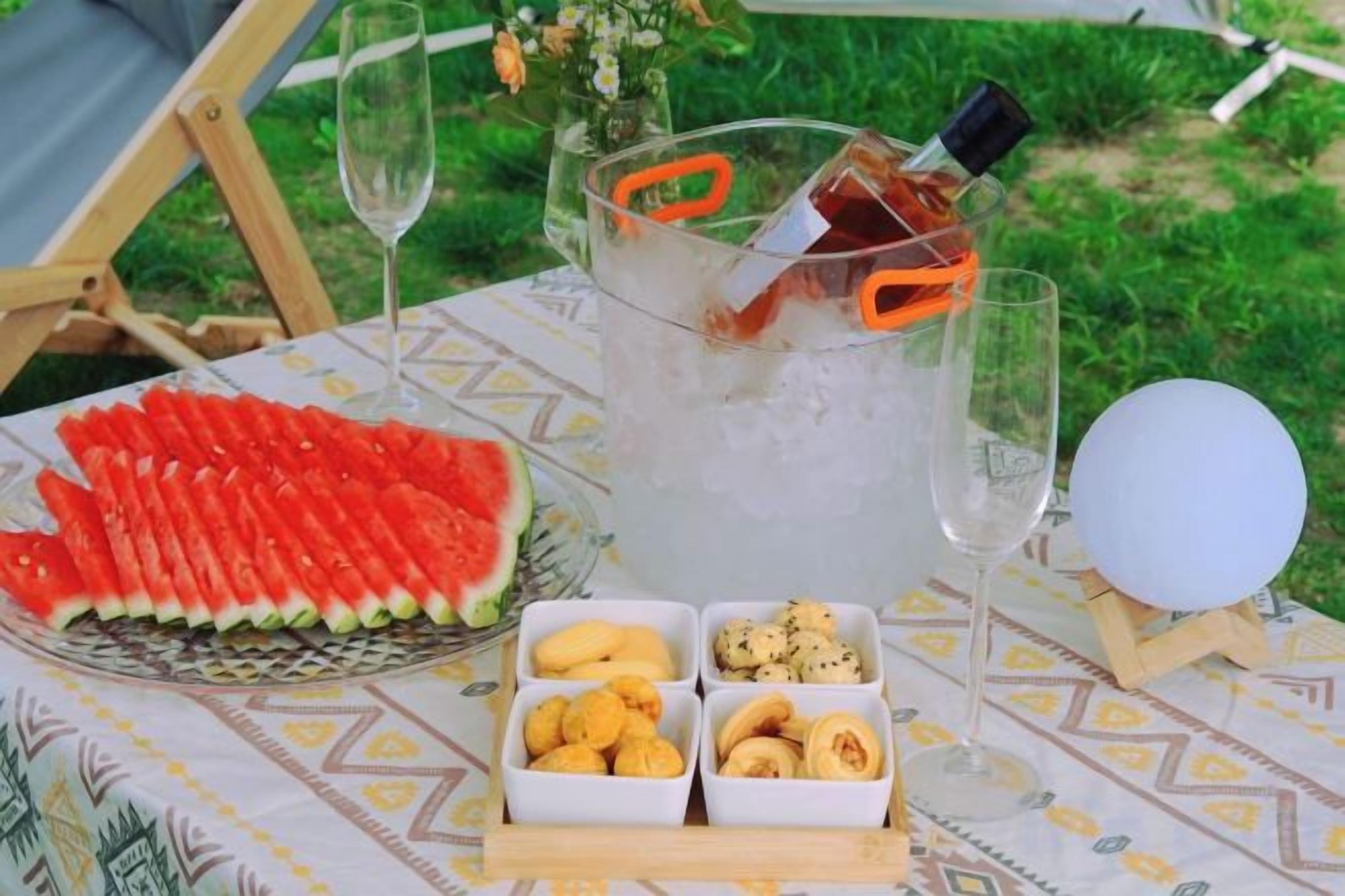 Ein Tisch mit Wassermelone, Eis, einer Flasche, Gläsern und Snacks.