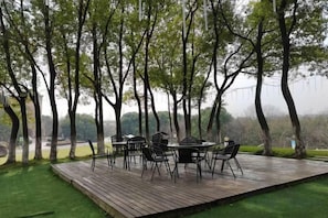 Un espace extérieur aménagé pour les repas, avec une terrasse en bois, entouré d’arbres et offrant une vue sur le paysage.