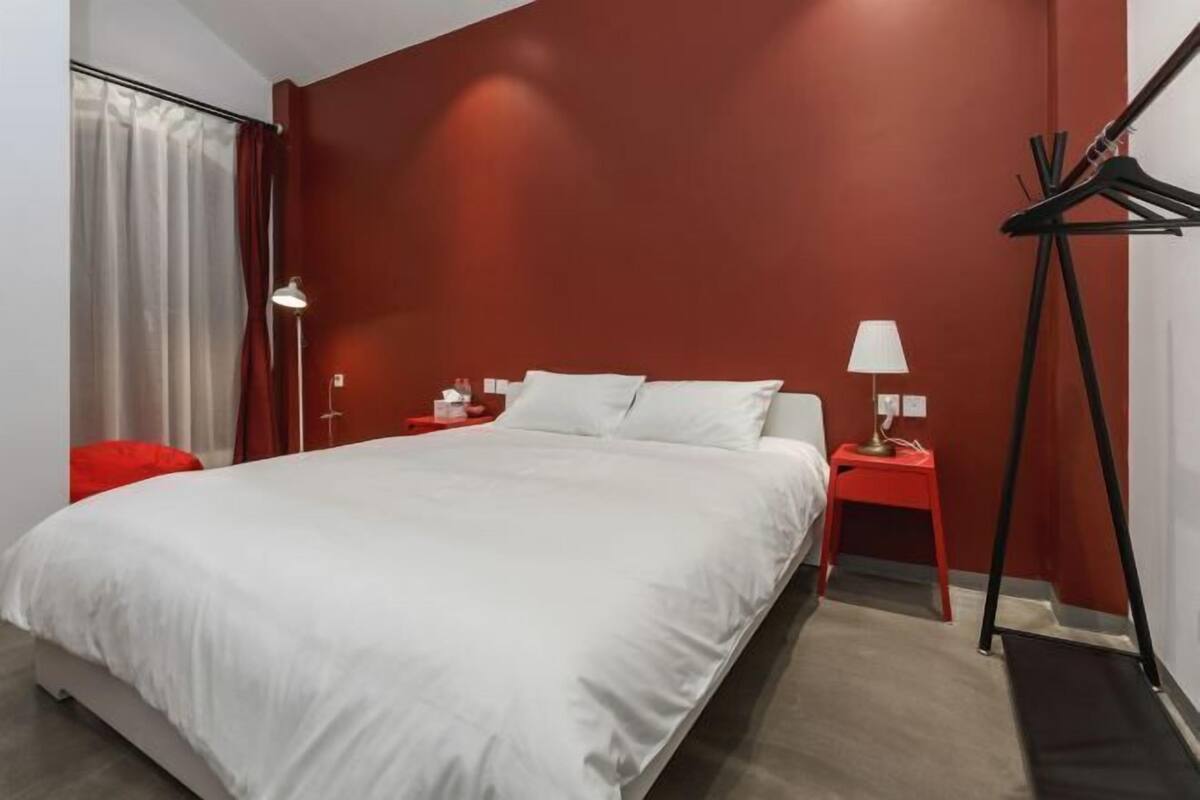 Una habitación de hotel moderna con una cama grande, detalles en rojo y dos mesitas de noche con lámparas.
