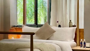 Una habitación de hotel con cama, mesita de noche, ventana con vistas a zonas verdes y una lámpara.