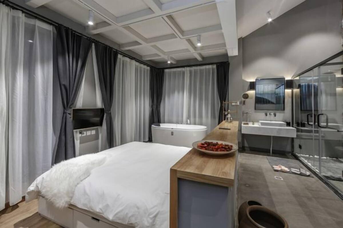 Un dormitorio moderno con cama, tocador con espejo, bañera y televisión.