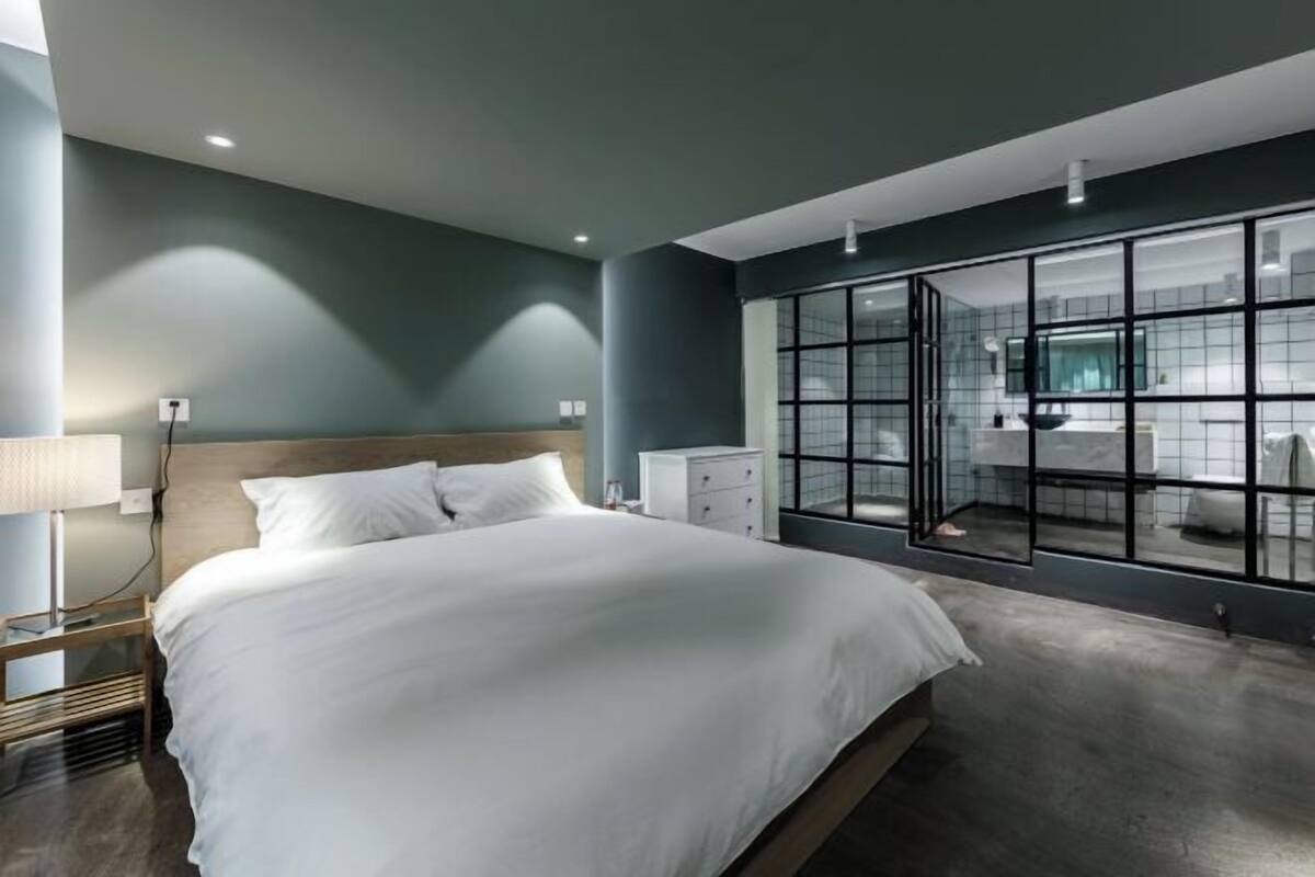 Una habitación de hotel moderna con una cama grande, una mesita de noche, un armario y un muro divisorio de vidrio.