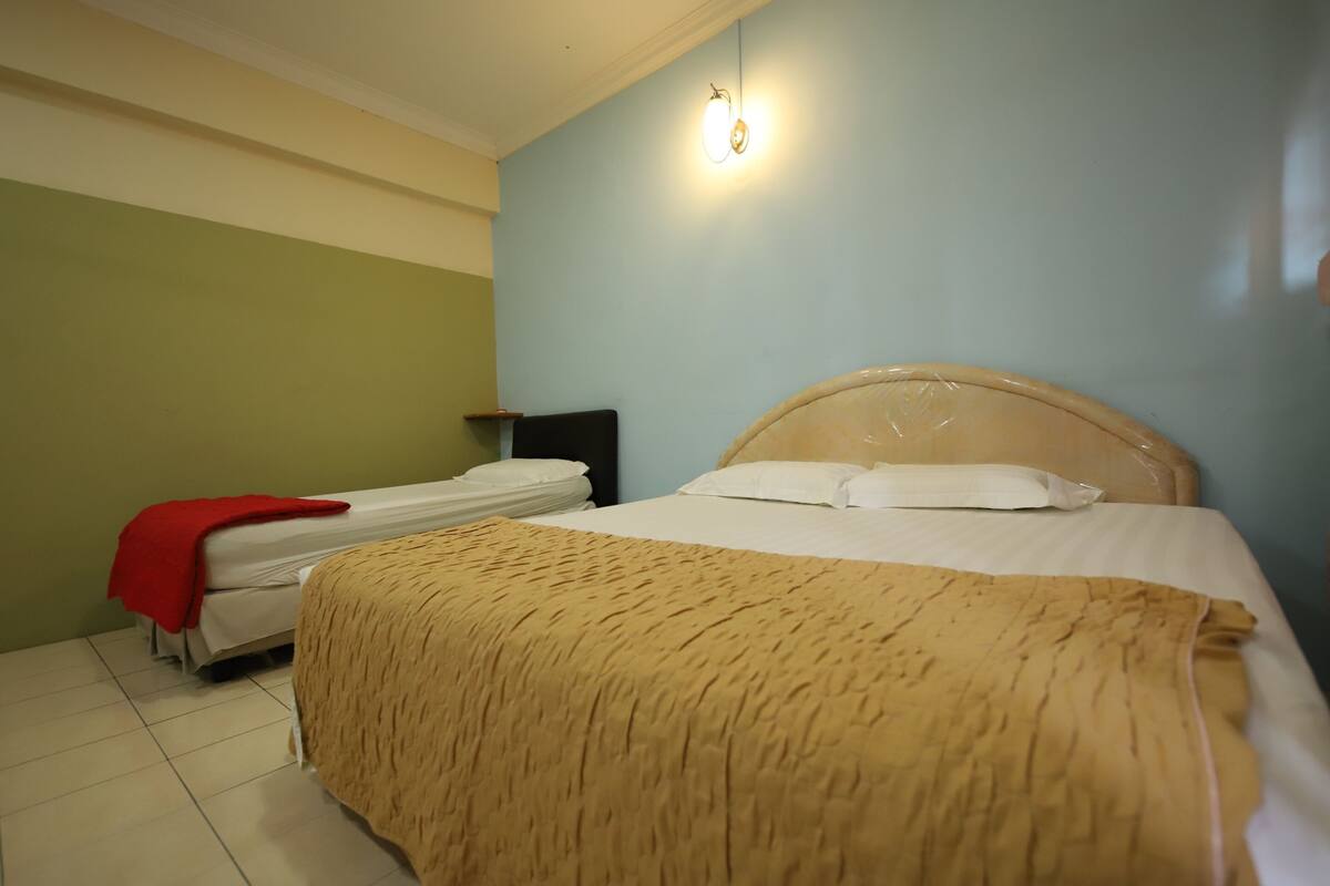 Una habitación de hotel con una cama grande, una cama más pequeña y una mesita de noche con una lámpara.