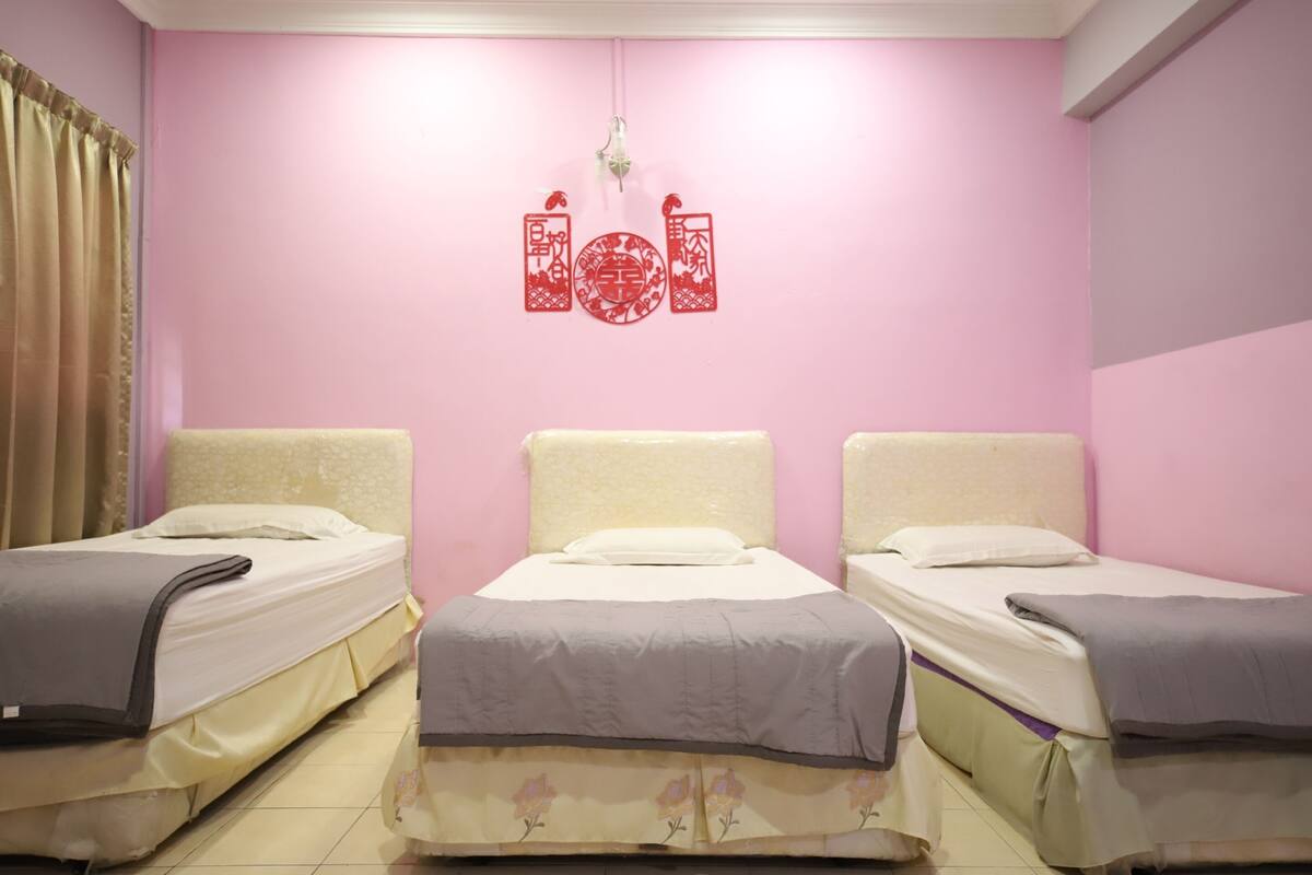 Una habitación con tres camas, paredes rosas y un adorno rojo colgante.