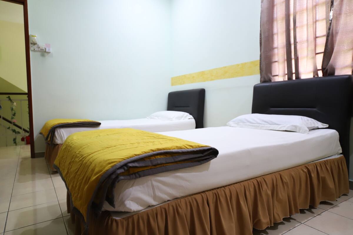 Habitación de hotel con dos camas, cada una con una manta amarilla y falda marrón.