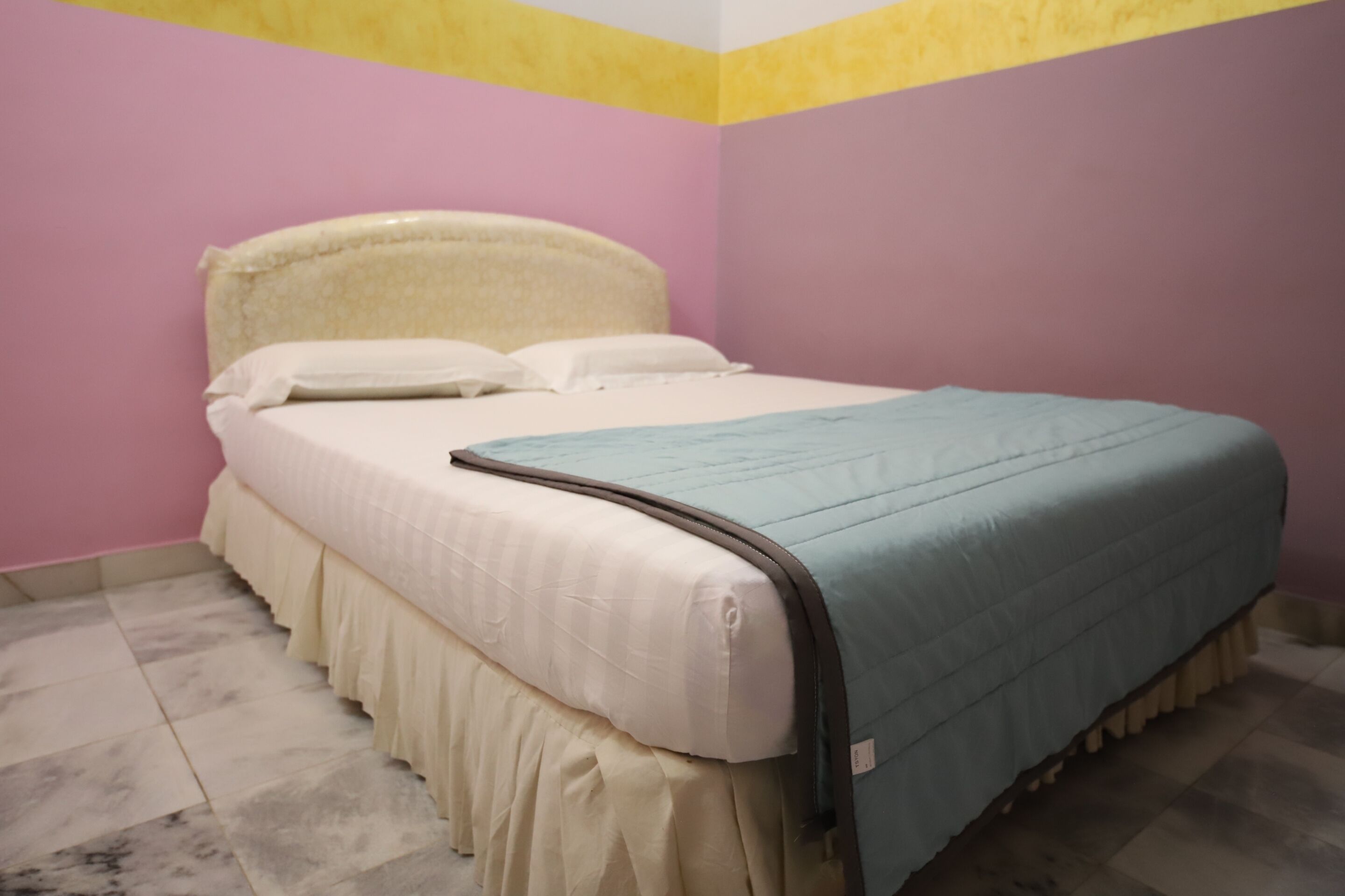 A bed with a white headboard and a blue blanket in a room with pink walls and a yellow ceiling.