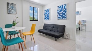 A modern living room with a black sofa, teal and yellow chairs, a white table, and abstract art on the walls.