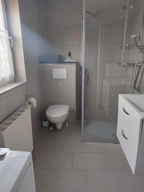 A bathroom with a toilet, a shower, and a sink. - Vacation apartment Baltic Sea (Rethwisch)