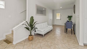 Un intérieur épuré et moderne, avec un escalier blanc, un canapé blanc, une table à manger avec des chaises et une plante en pot.