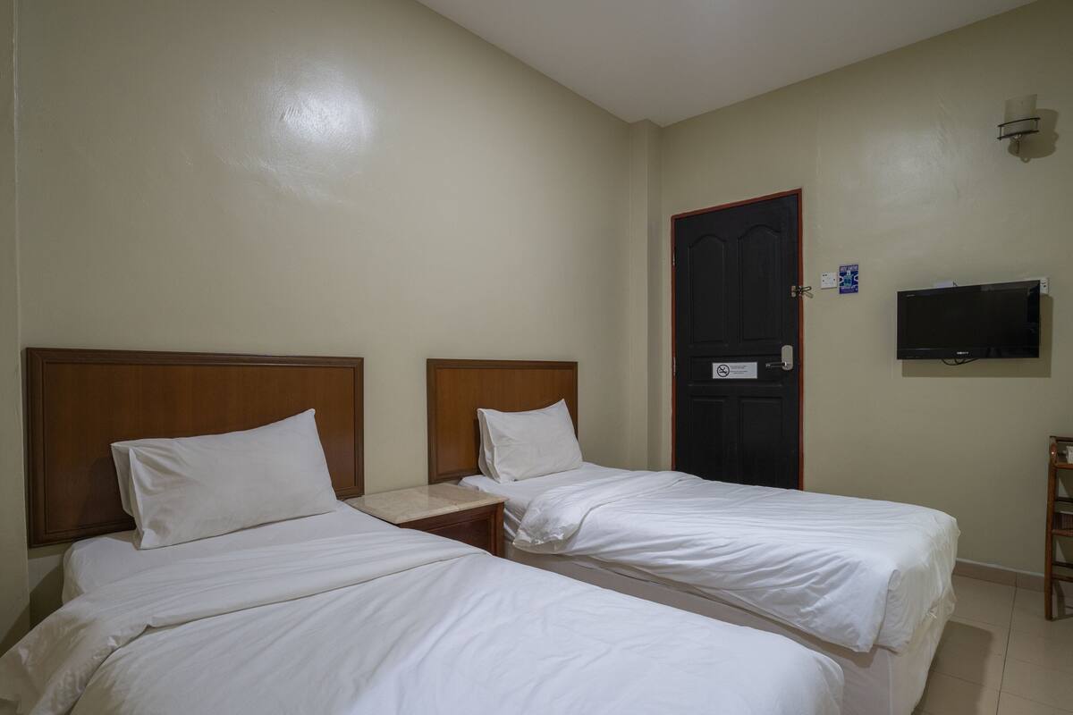 A hotel room with two single beds, a wooden headboard, a nightstand, a TV mounted on the wall, and a door with a sign.