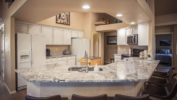 A modern kitchen with white cabinets, a granite countertop, and a central island with seating. - Epic McCall Home Built for Serious Group Fun! (McCall)