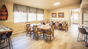 A dining area with wooden tables and chairs, a kitchen area with a refrigerator, and a hallway leading to another room. - Epic McCall Home Built for Serious Group Fun! (McCall)