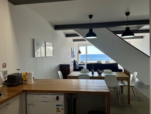 A modern kitchen with a Bosch dishwasher, a dining area with a wooden table and white chairs, and a view of the ocean through a large window.