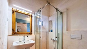 Een badkamer met een douchecabine van glas, een witte wastafel met een spiegel met gouden lijst, en een wit toilet.
