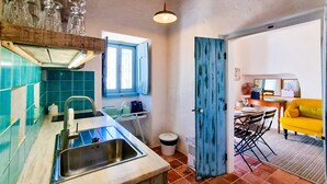 Een keuken met een spoelbak, een raam en een deur die leidt naar een eethoek met een gele bank.