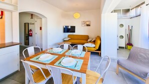 Un salon moderne avec un canapé, une table à manger pour quatre personnes et un téléviseur fixé au mur.