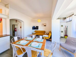 A modern living room with a sofa, a dining table set for four, and a TV mounted on the wall.