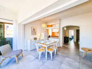 A modern kitchen with white cabinets, a dining area with a wooden table and white chairs, and a view of a balcony.