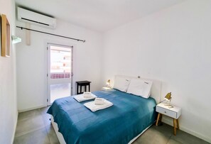 Un dormitorio con cama, mesitas de noche, un equipo de aire acondicionado y vistas por una puerta.