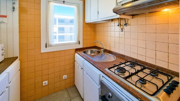 Une cuisine de taille réduite, équipée d’une cuisinière à gaz, d’un évier et d’une fenêtre.
