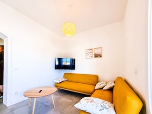 Una sala de estar moderna con un sofá amarillo, una mesita de madera, un televisor de pantalla plana y una lámpara decorativa.