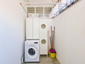 A laundry room with a washing machine, a broom, and a mop.