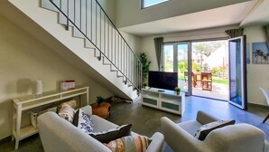 Sala de estar moderna com escada, TV de tela plana e porta de vidro deslizante que dá para um pátio externo.