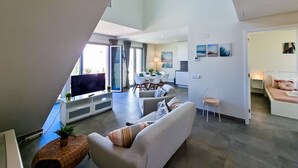 Uma sala de estar moderna com um sofá, uma televisão e uma área de jantar com uma mesa e cadeiras.