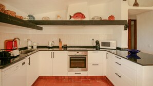 Eine Küche mit weißen Schränken, einem Edelstahlbackofen, einer Mikrowelle und einem roten Wasserkocher.